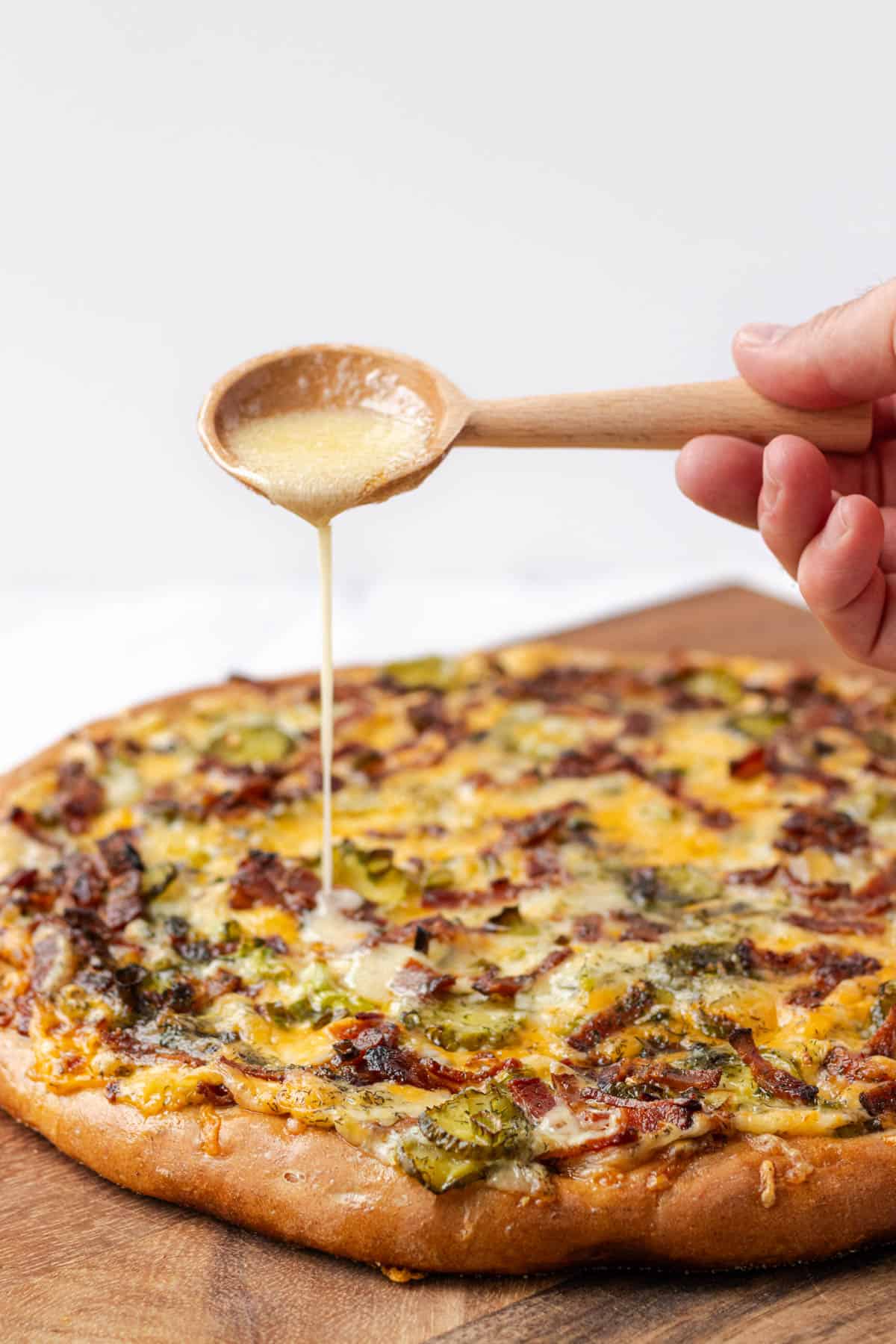 Drizzling melted honey butter over the cooked pizza with a wooden spoon.