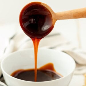 Eel sauce dripping off of a wooden spoon into a white bowl.