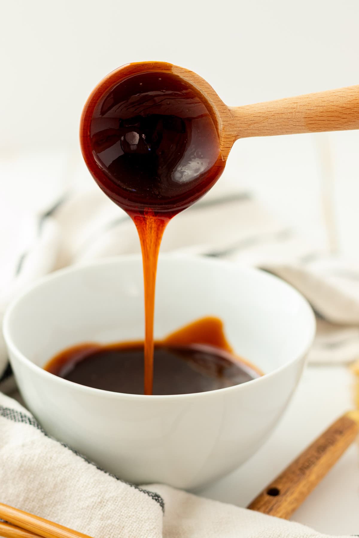 Eel sauce dripping off of a wooden spoon into a white bowl.