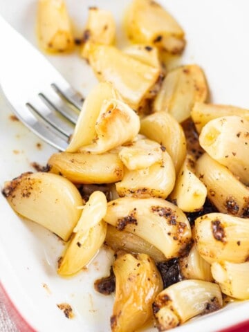 Whole golden brown roasted garlic cloves in a dish with a fork.