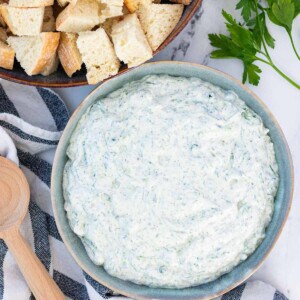 A blue serving bowl filled with spinach dip with a bowl of sourdough bread for dipping on the side.