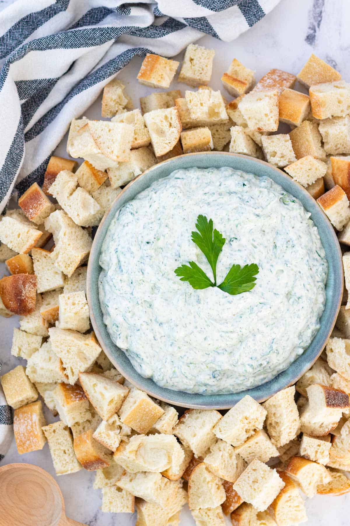 A large blue serving bowl filled with spinach dip surrounded by chunks of sourdough bread.