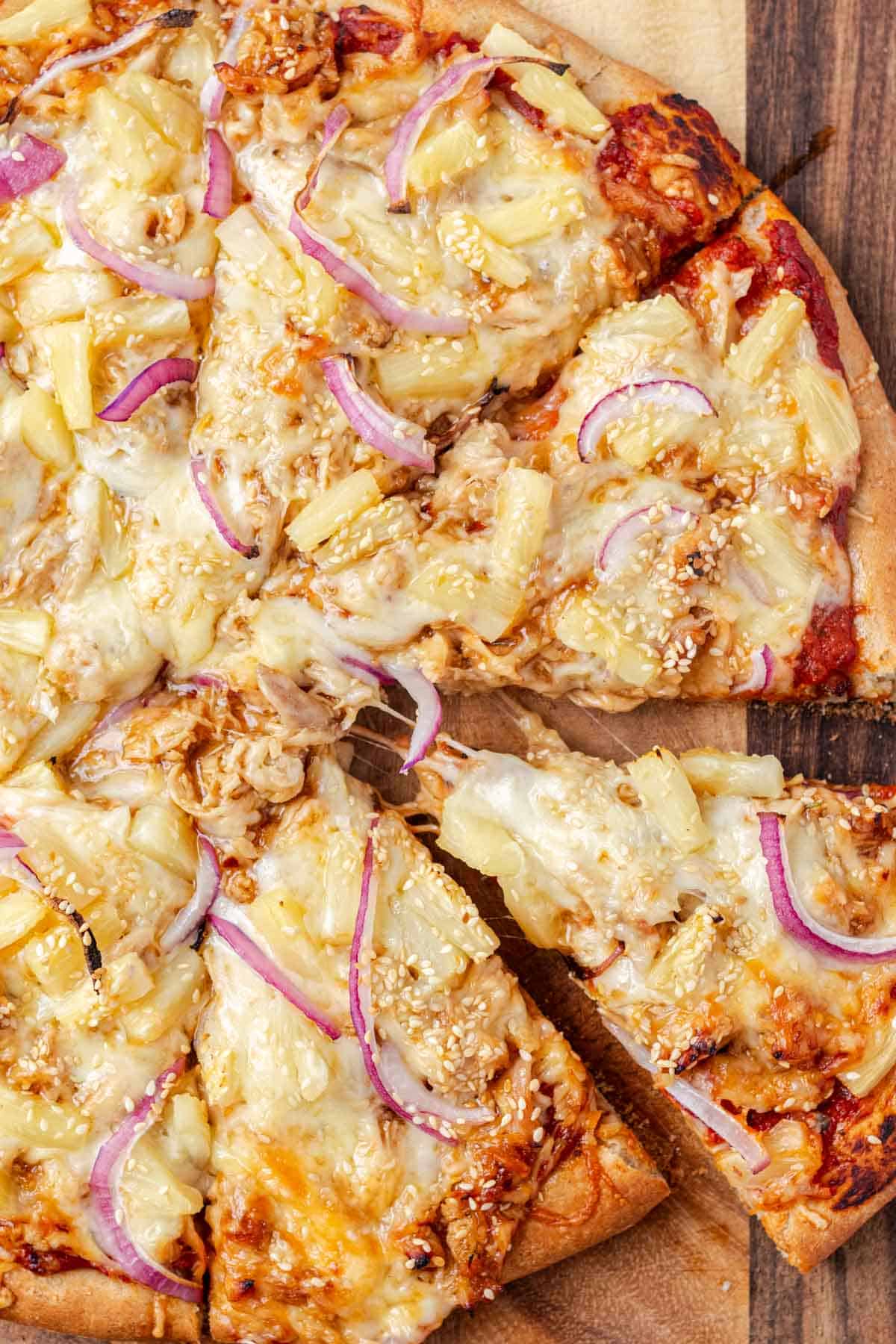 A slice of teriyaki chicken and pineapple pizza being pulled out.