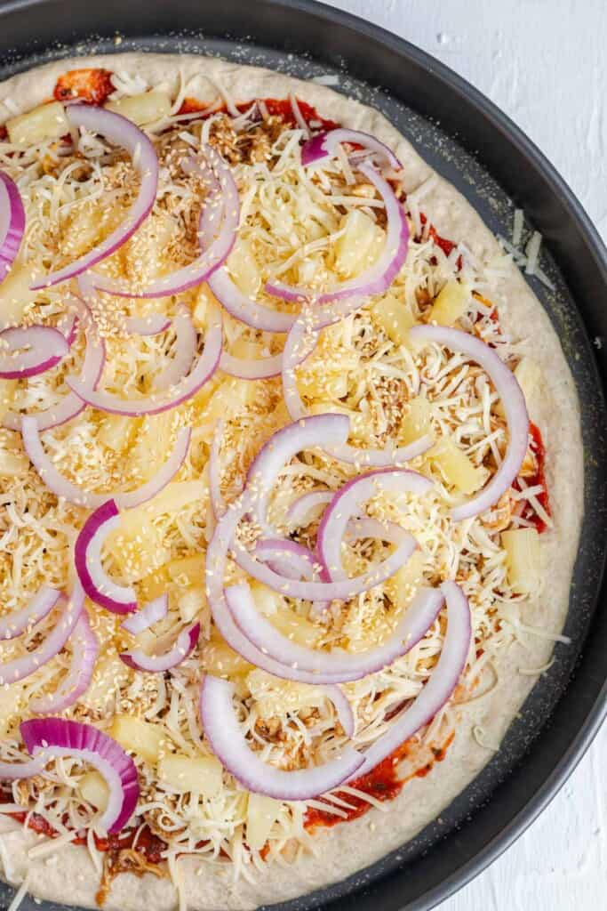 Adding pineapples, red onions, toasted sesame seeds and more cheese on top of the pizza.