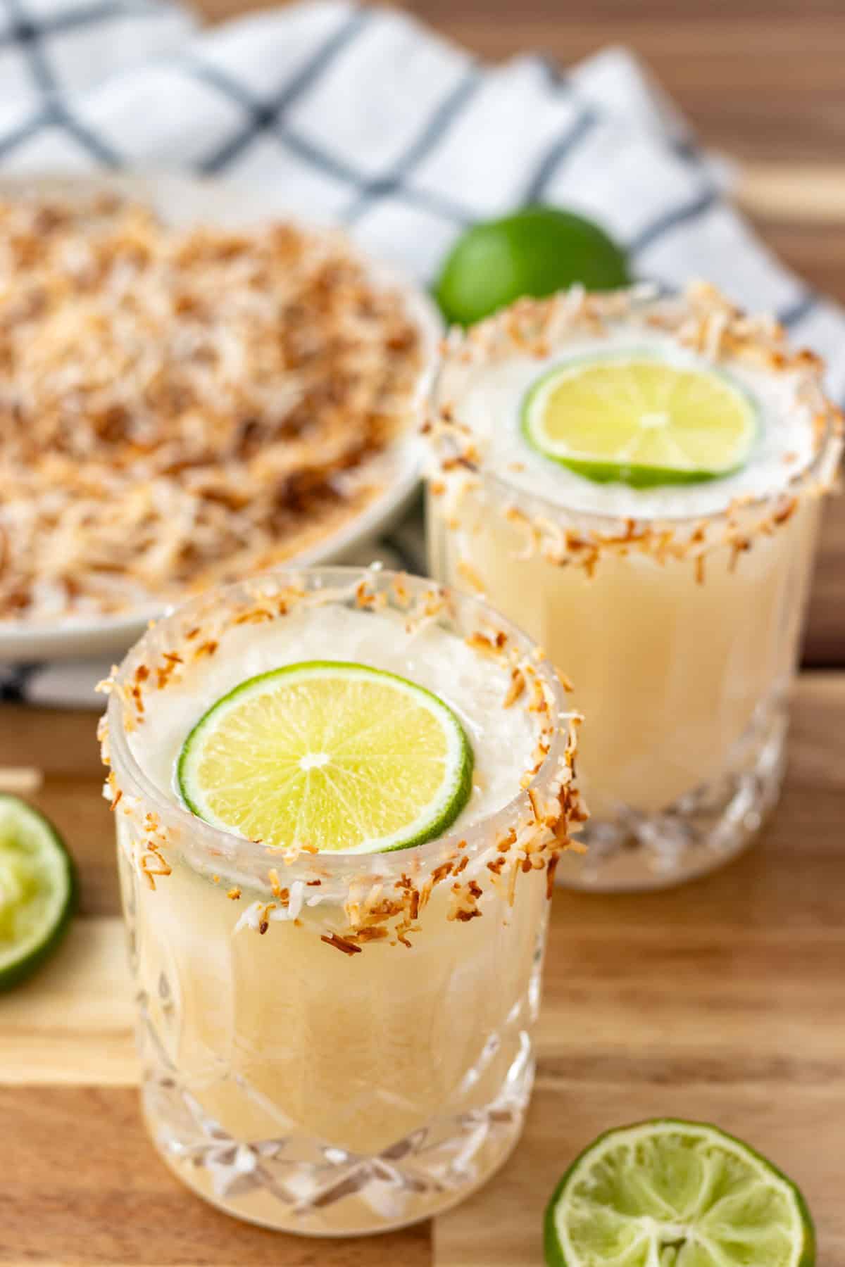 Two coconut margaritas rimmed with toasted coconut and topped with a wheel of lime.