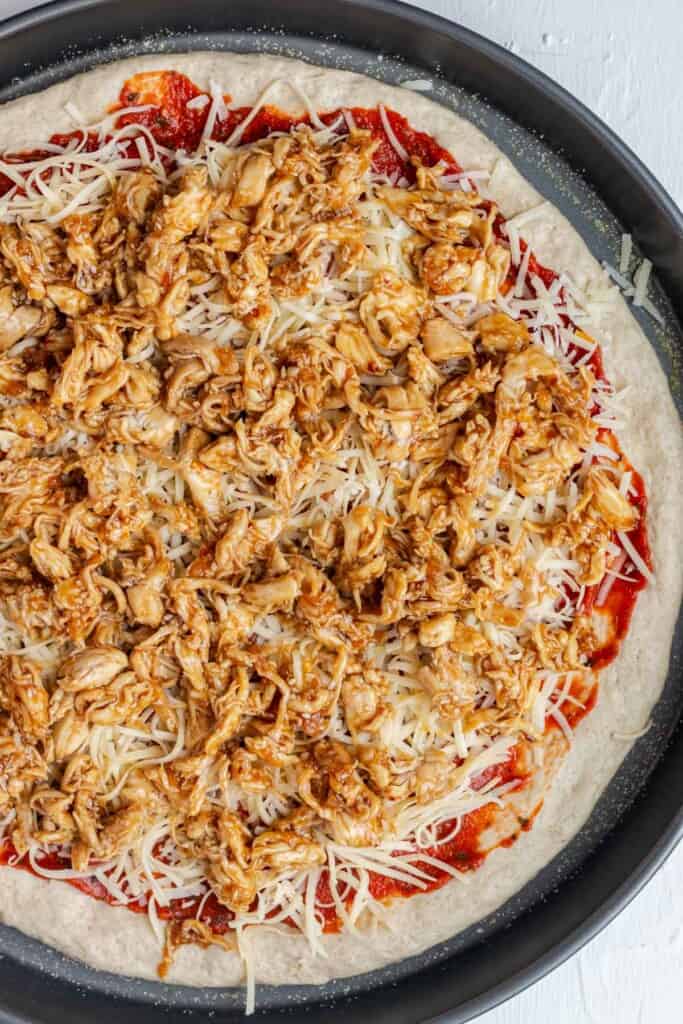 Adding the cheese and teriyaki chicken on top of the marinara sauce.