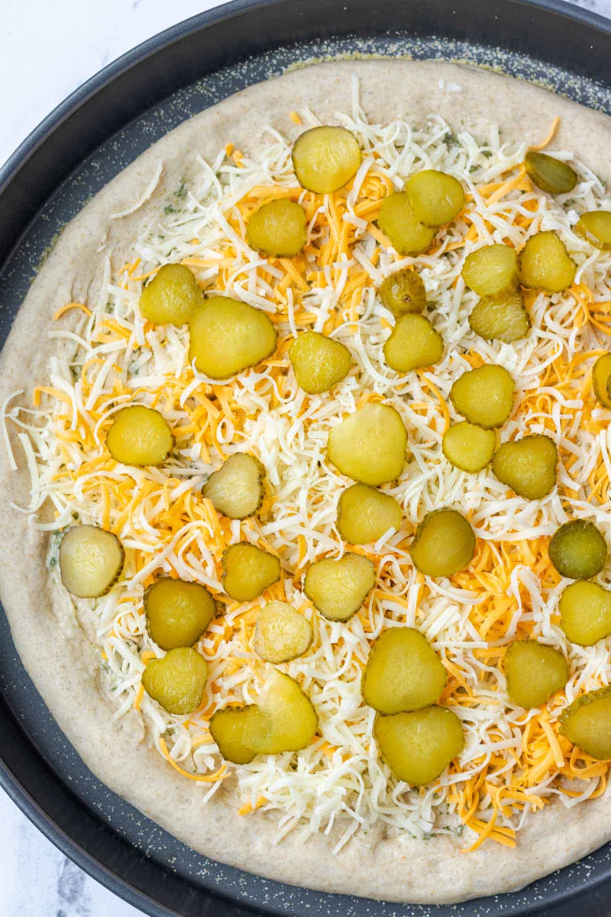 Layering cheese and dill pickles on to the pizza crust.
