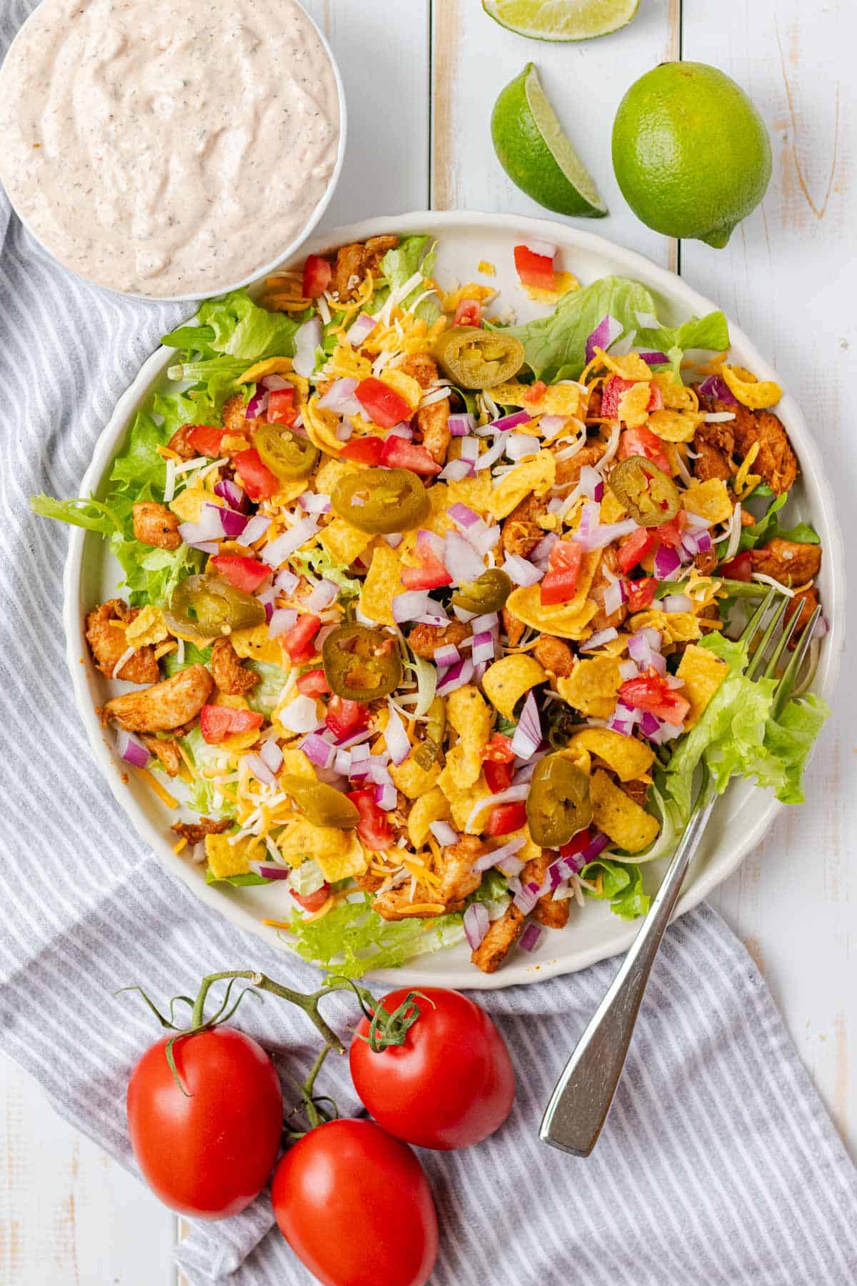 A white plate filled with chicken taco salad with dressing on the side.