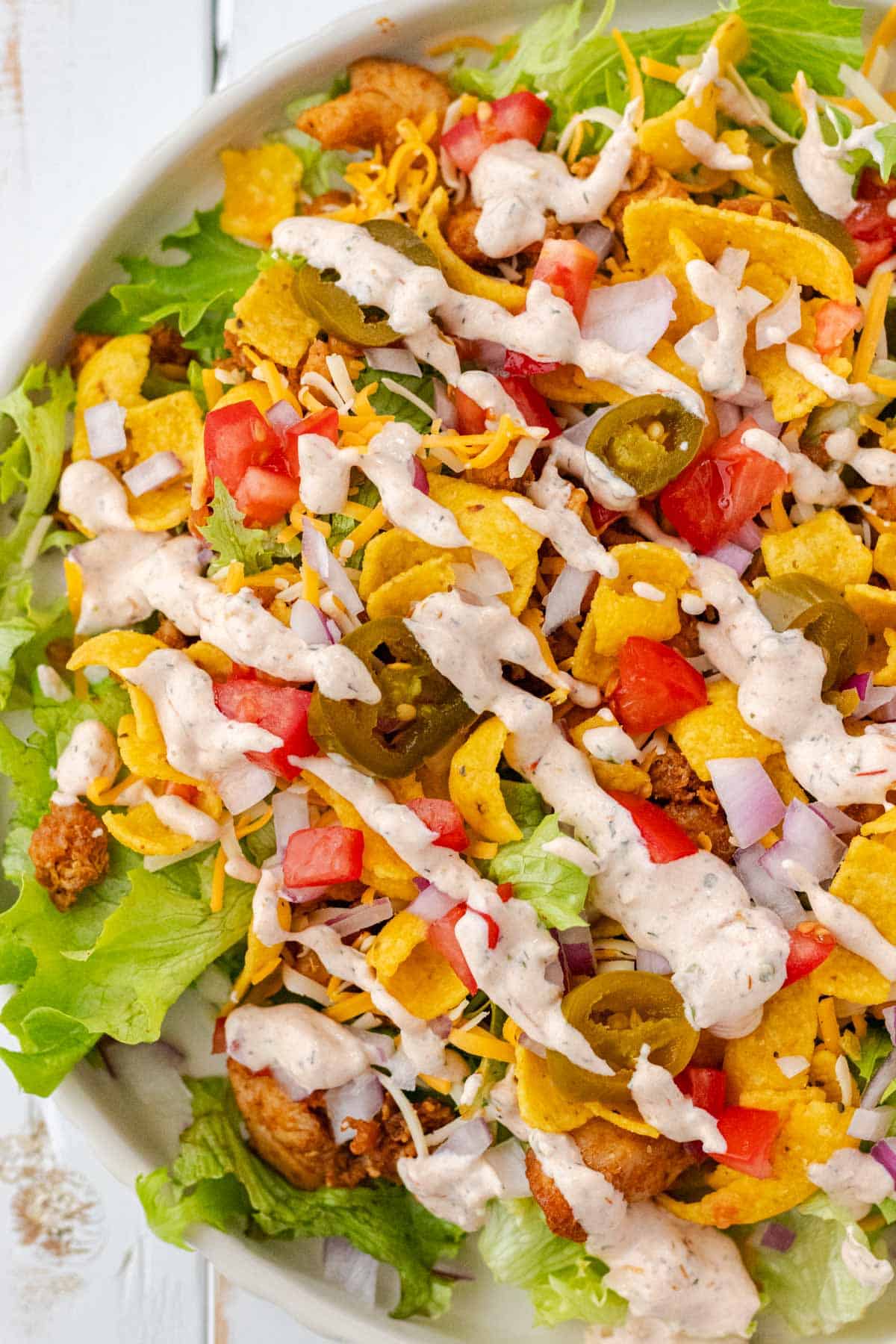Close-up shot of half a plate filled with chicken taco salad and topped with dressing.