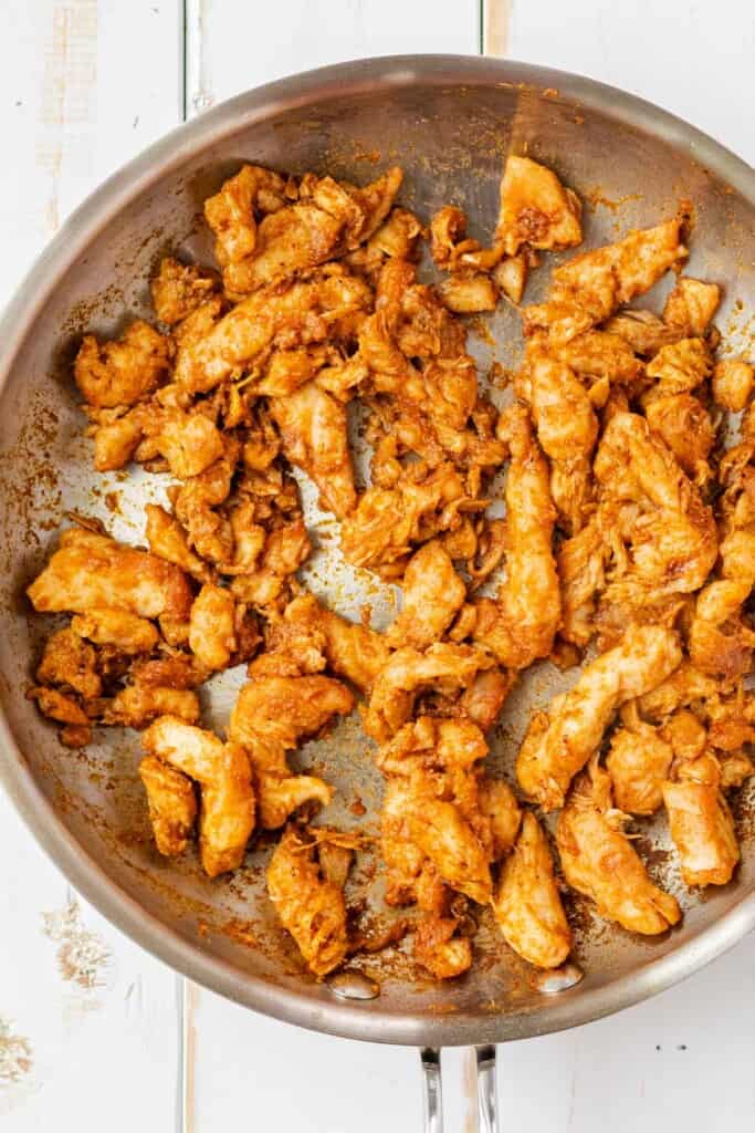 A stainless steel frying pan full of chicken cooked in taco seasoning.