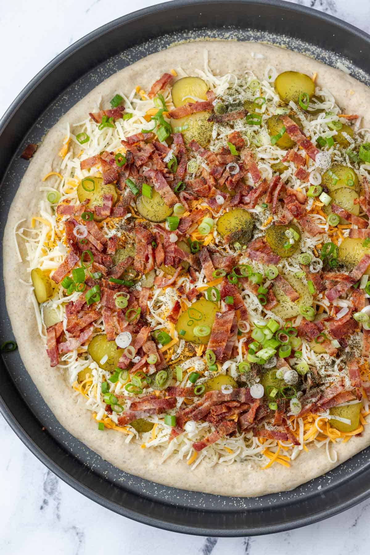 Adding the bacon, green onions, dill, and remaining cheese to the pizza.