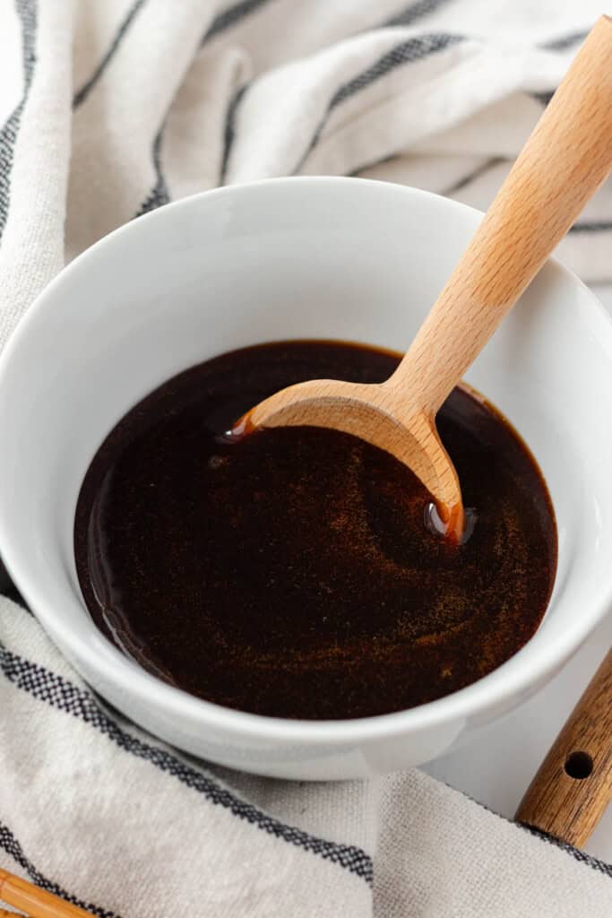A white bowl full of eel sauce with a wooden serving spoon in it.