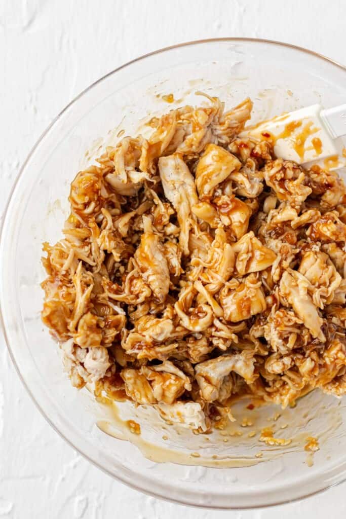 Tossing the shredded chicken with teriyaki sauce.