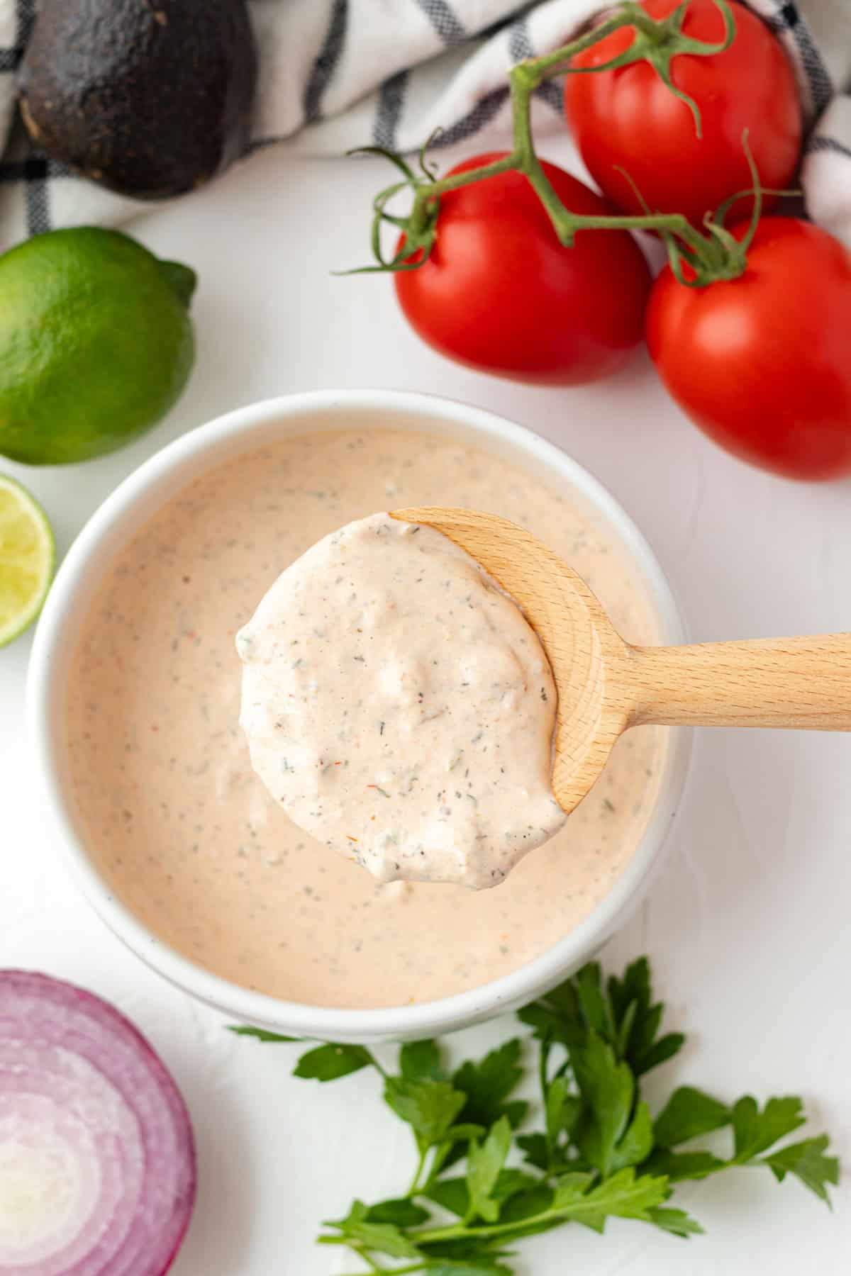 A wooden spoonful of taco salad dressing hovering over a full bowl of dressing.