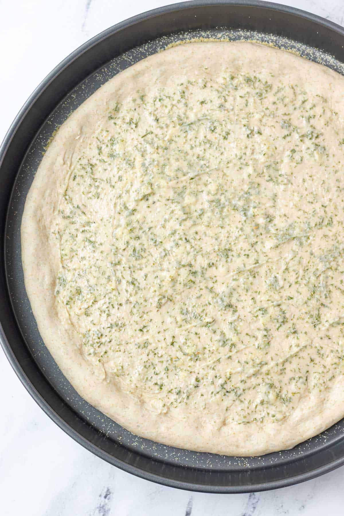 Spreading garlic butter overtop of the pressed pizza dough.