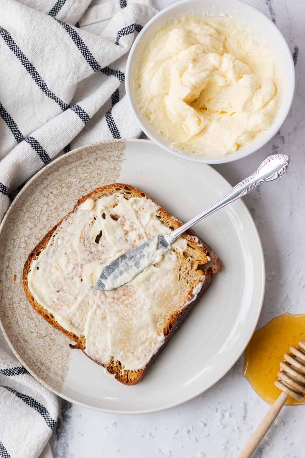 A piece of toasted sourdough bread being spread with thick honey butter.