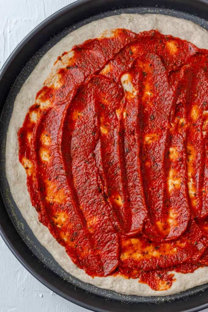 Spreading marinara sauce onto a pizza crust on a pizza pan.