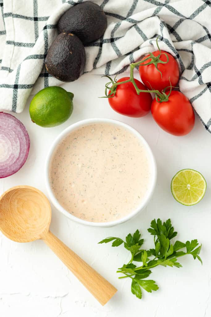 A bowl full of taco salad dressing surrounded by taco salad toppings.