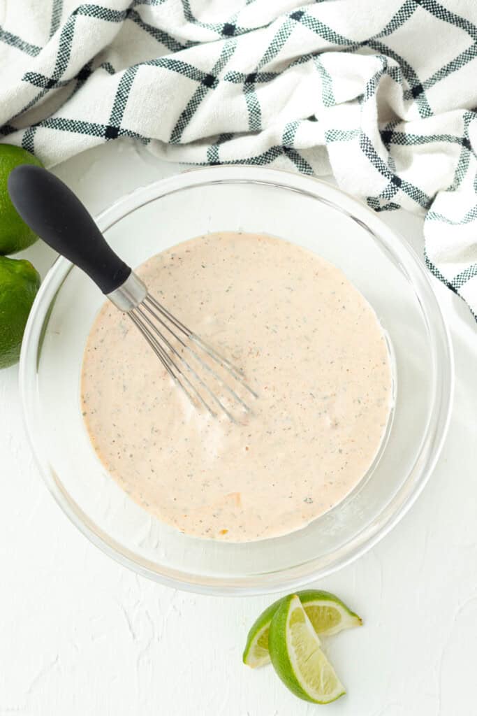 Mixing the dressing with a whisk in a glass bowl.