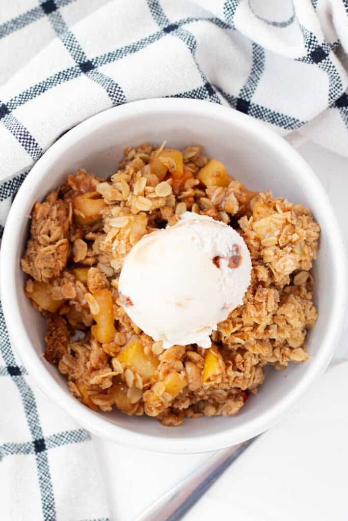 A white bowl with a serving of apple crisp, topped with a scoop of ice cream.