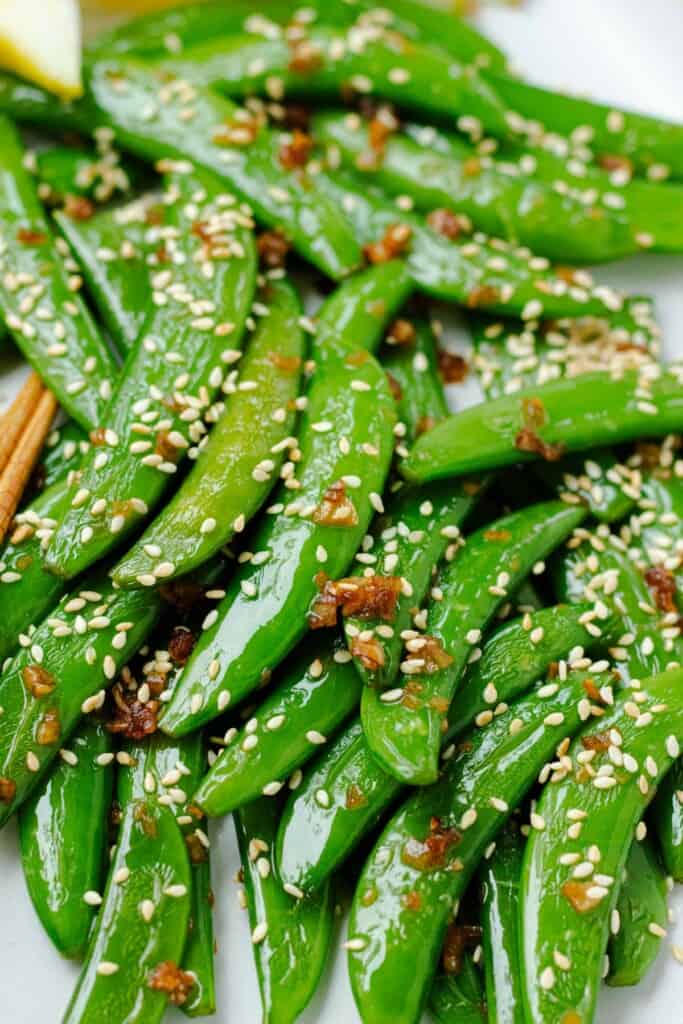 A close up of snow peas topped with garlic and toasted sesame seeds.