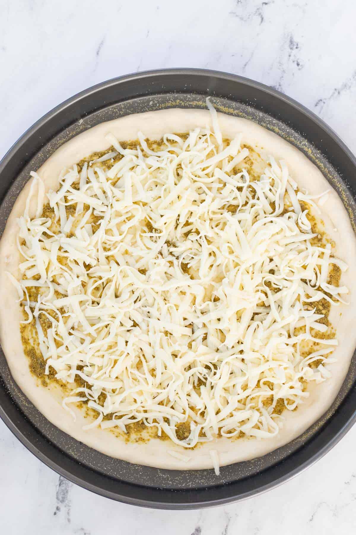 Adding shredded mozzarella cheese to the pizza crust.