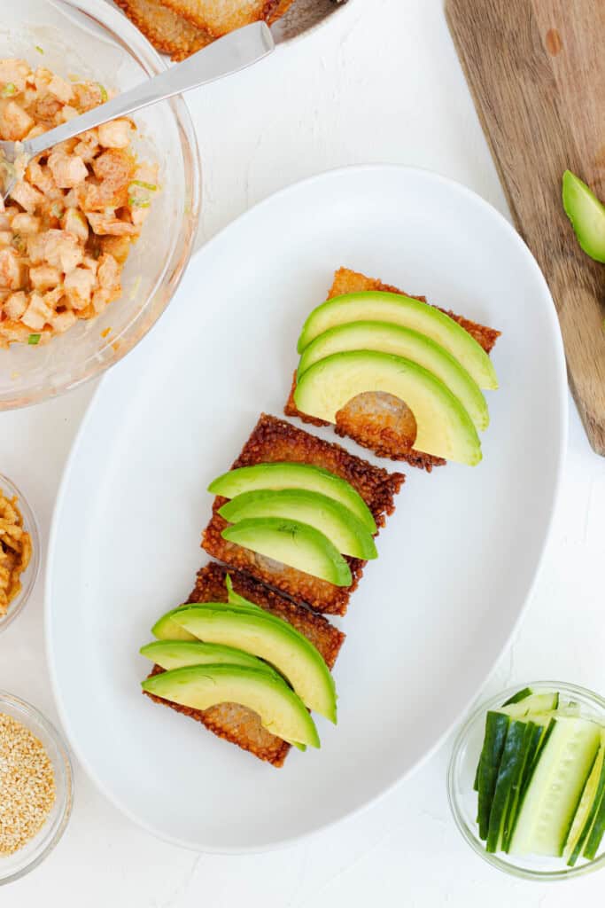 Building the sushi bites by laying out crispy rice squares and topping them with thinly sliced avocado.