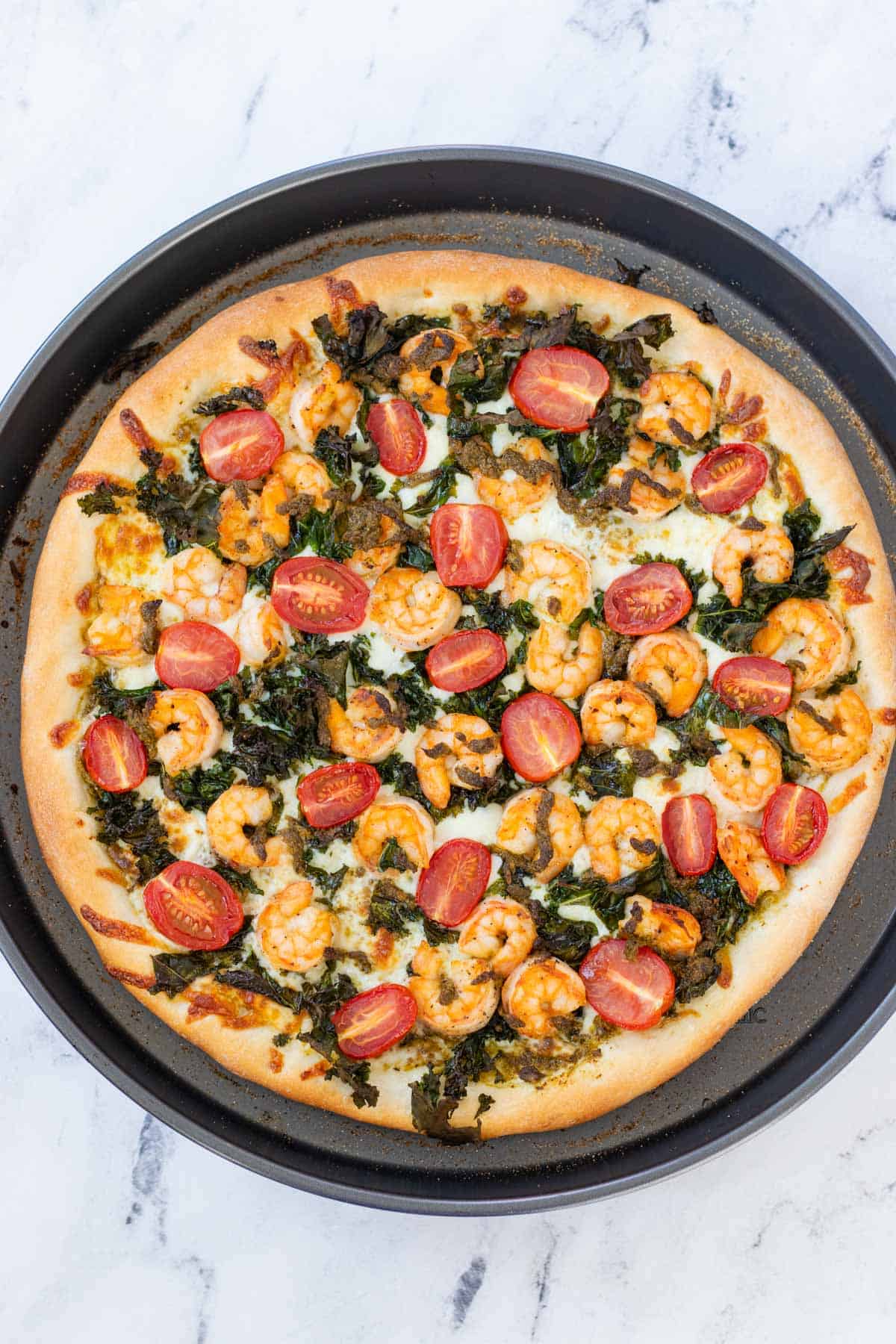 Golden brown, baked prawn and pesto pizza in a circular pizza pan.