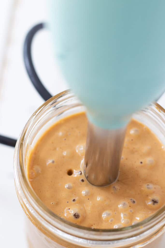 An immersion blender immersed in the jar of blended peanut sauce.