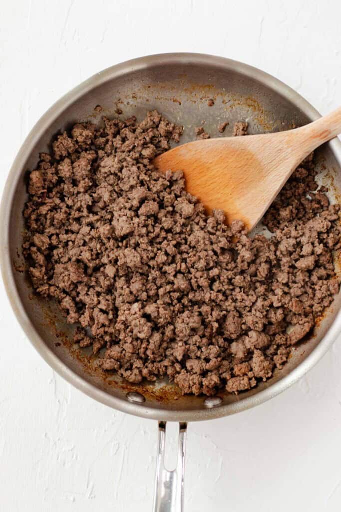 Browning the ground beef in a frying pan with a wooden spatula.