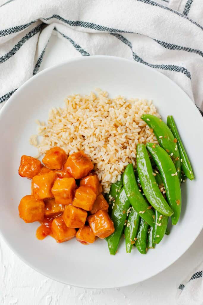 Building the bowls by adding brown rice, sautéed snow peas and sweet chili tofu.