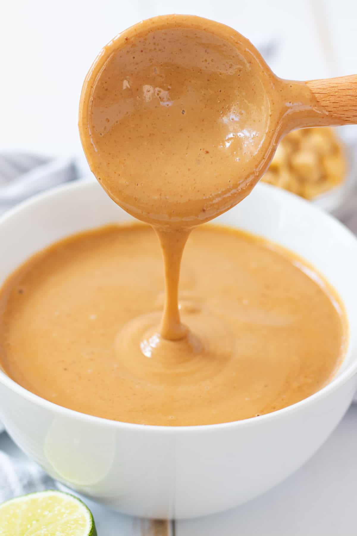 Peanut sauce drizzling off of a wooden spoon into a white bowl.