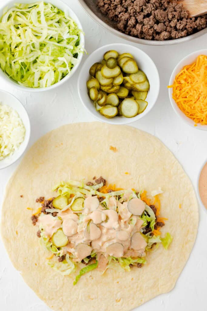 Adding the second layer of shredded lettuce, pickles, and special sauce on top.