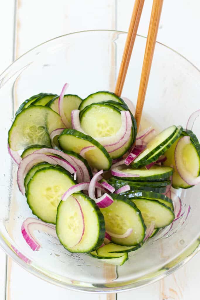 Mixing the quick pickled cucumber and red onion in a glass bowl.
