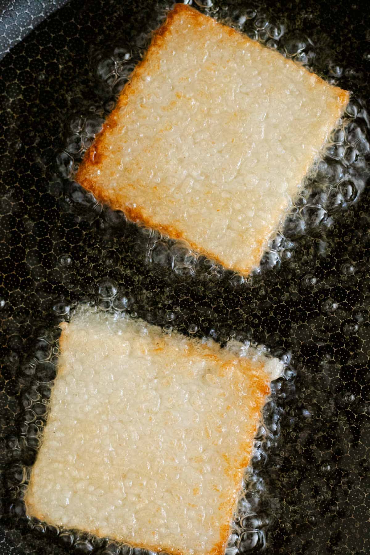 Frying two sushi rice cakes in hot oil.