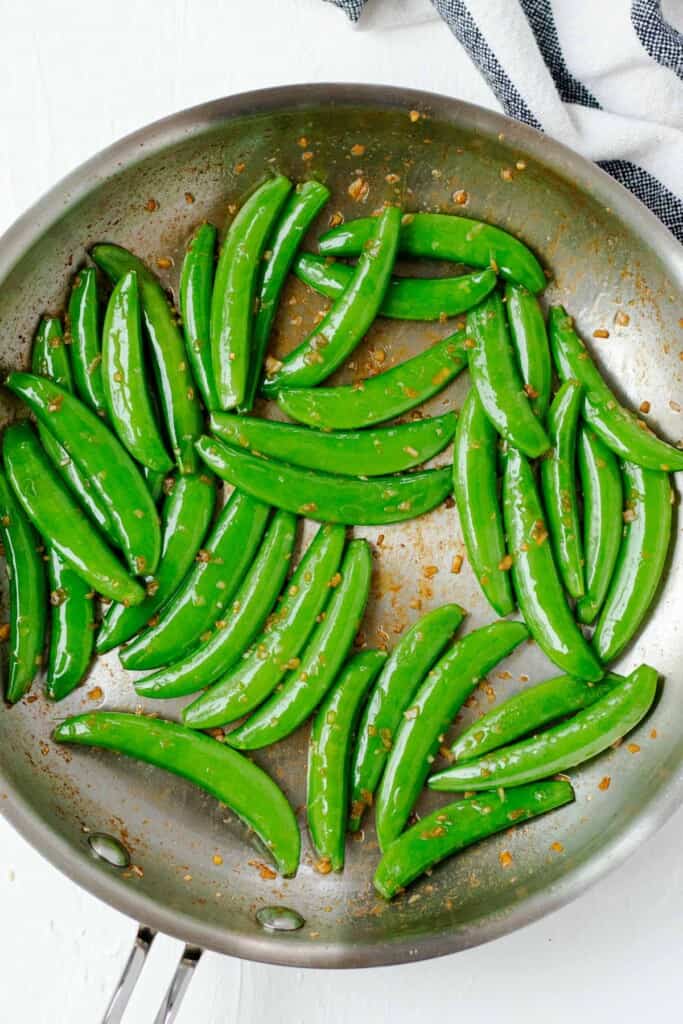 Frying snow peas in garlic, soy sauce, and sesame oil in a frying pan.