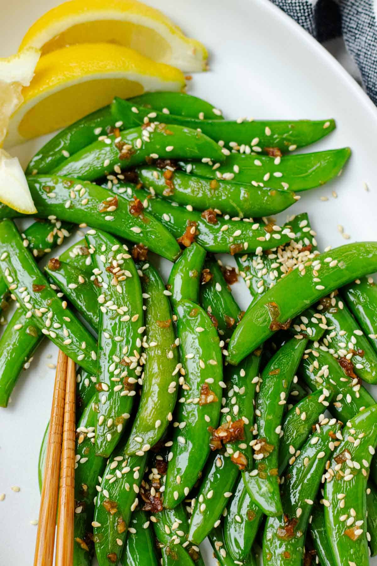 Garlic sesame snow peas with toasted sesame seeds on top on a white serving plate with lemons.
