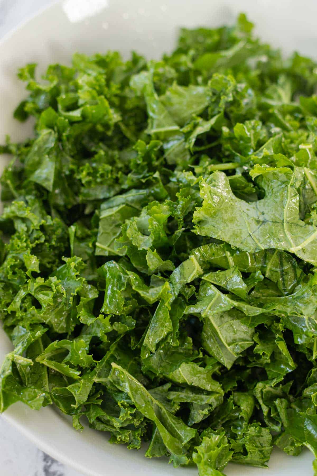 Kale rubbed with oil in a white bowl.