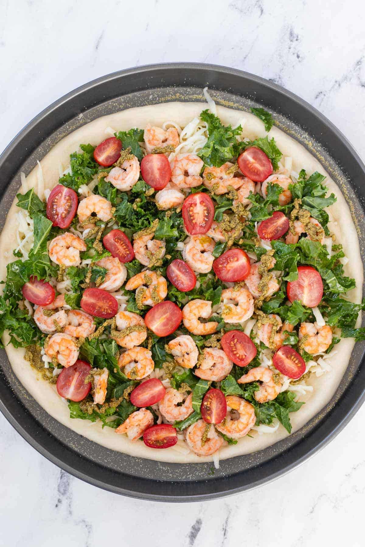 Kale, shrimp, tomatoes, and pesto drizzled onto the pizza.