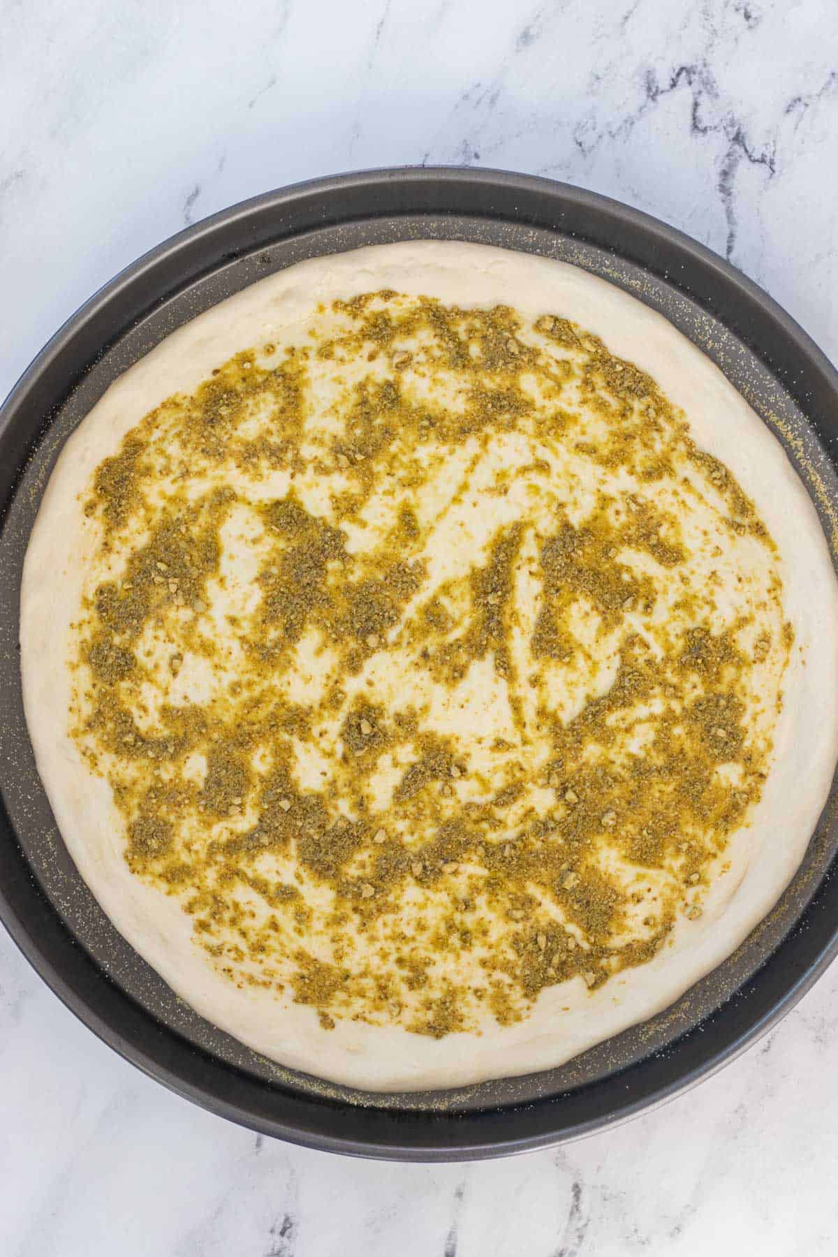 Pizza crust pressed into a pizza pan and topped with pesto.