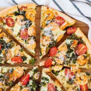 Prawn and pesto pizza cut into eight pieces on a wooden board.