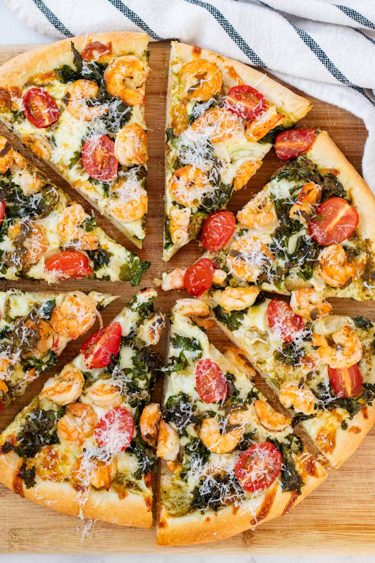 Prawn and pesto pizza cut into eight pieces on a wooden board.