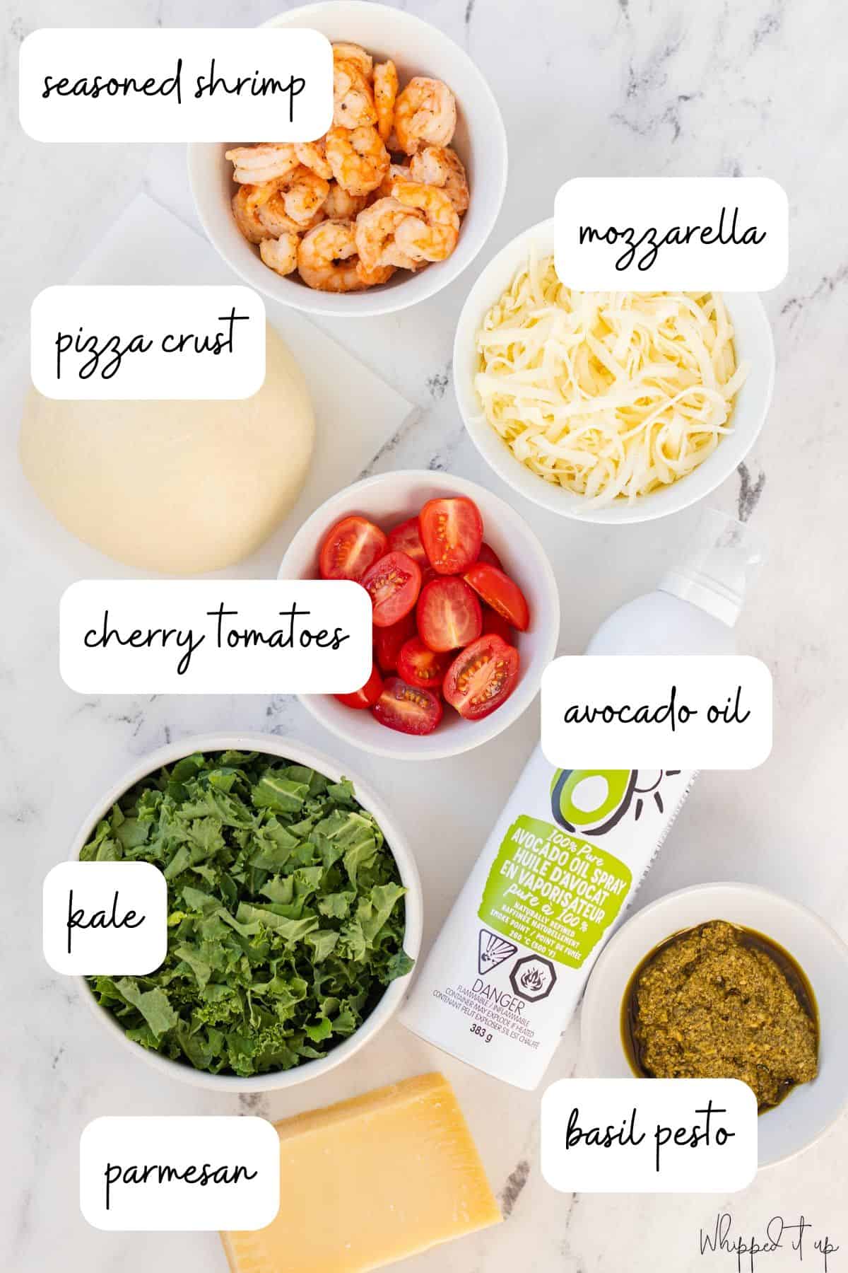 Ingredients include seasoned shrimp, mozzarella, pizza crust, cherry tomatoes, avocado oil, kale, basil pesto, and parmesan cheese.