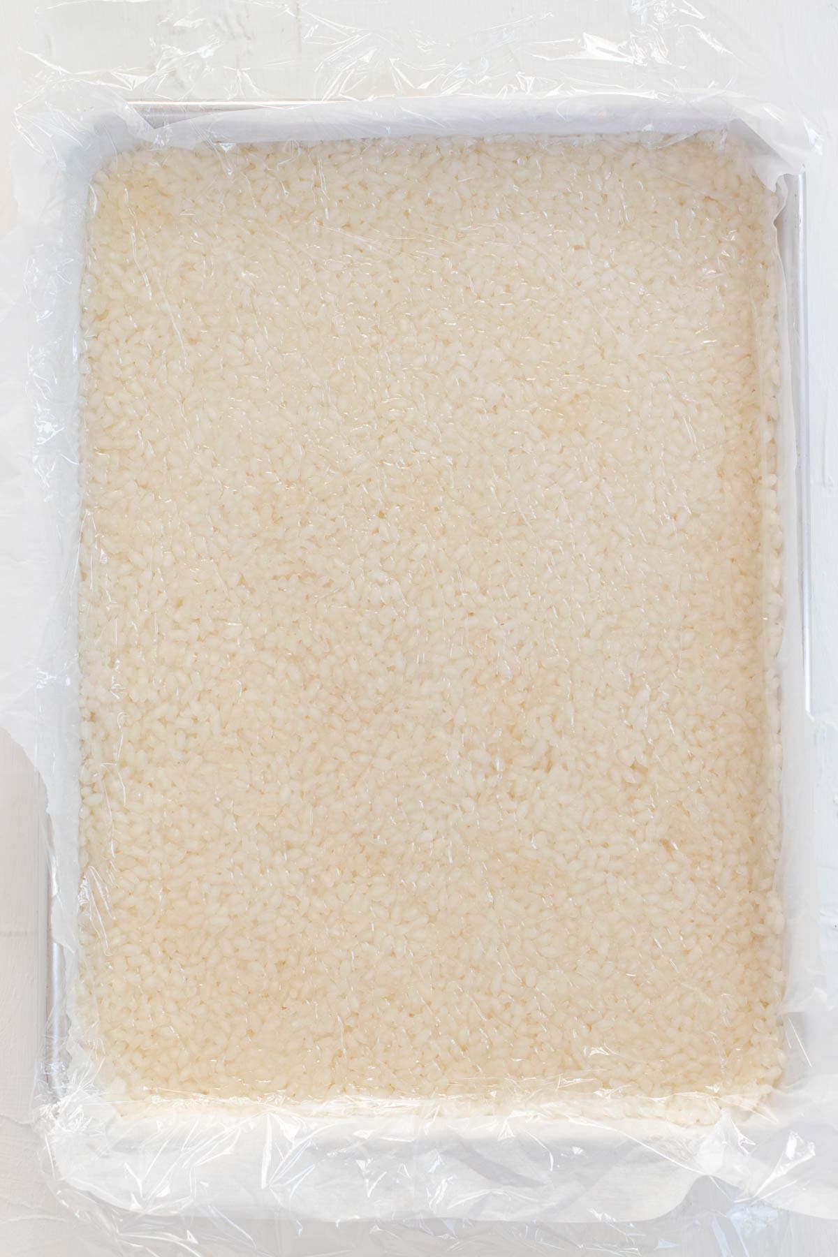 A pan full of pressed sushi rice covered tightly with plastic wrap.