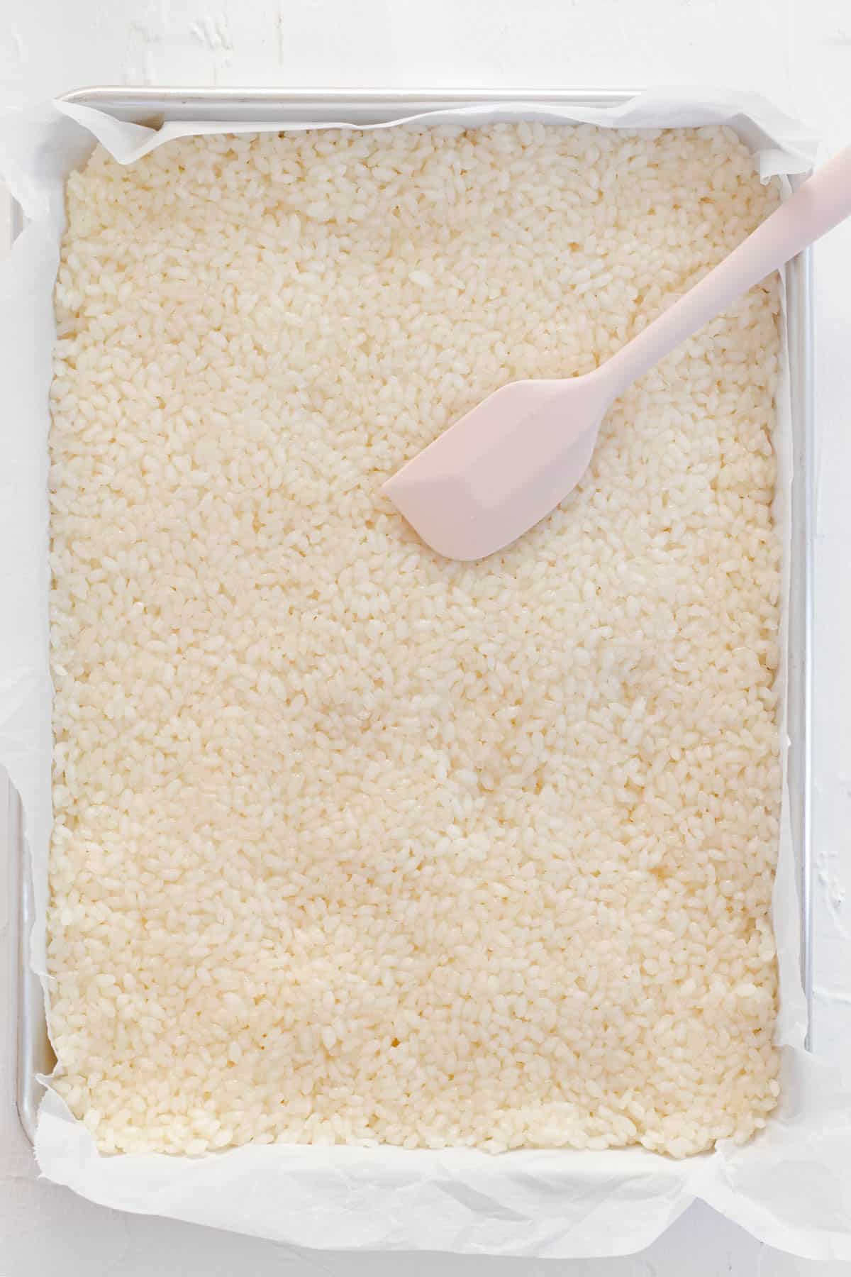 Spreading prepared and cooled sushi rice onto a quarter sheet pan lined with parchment paper.