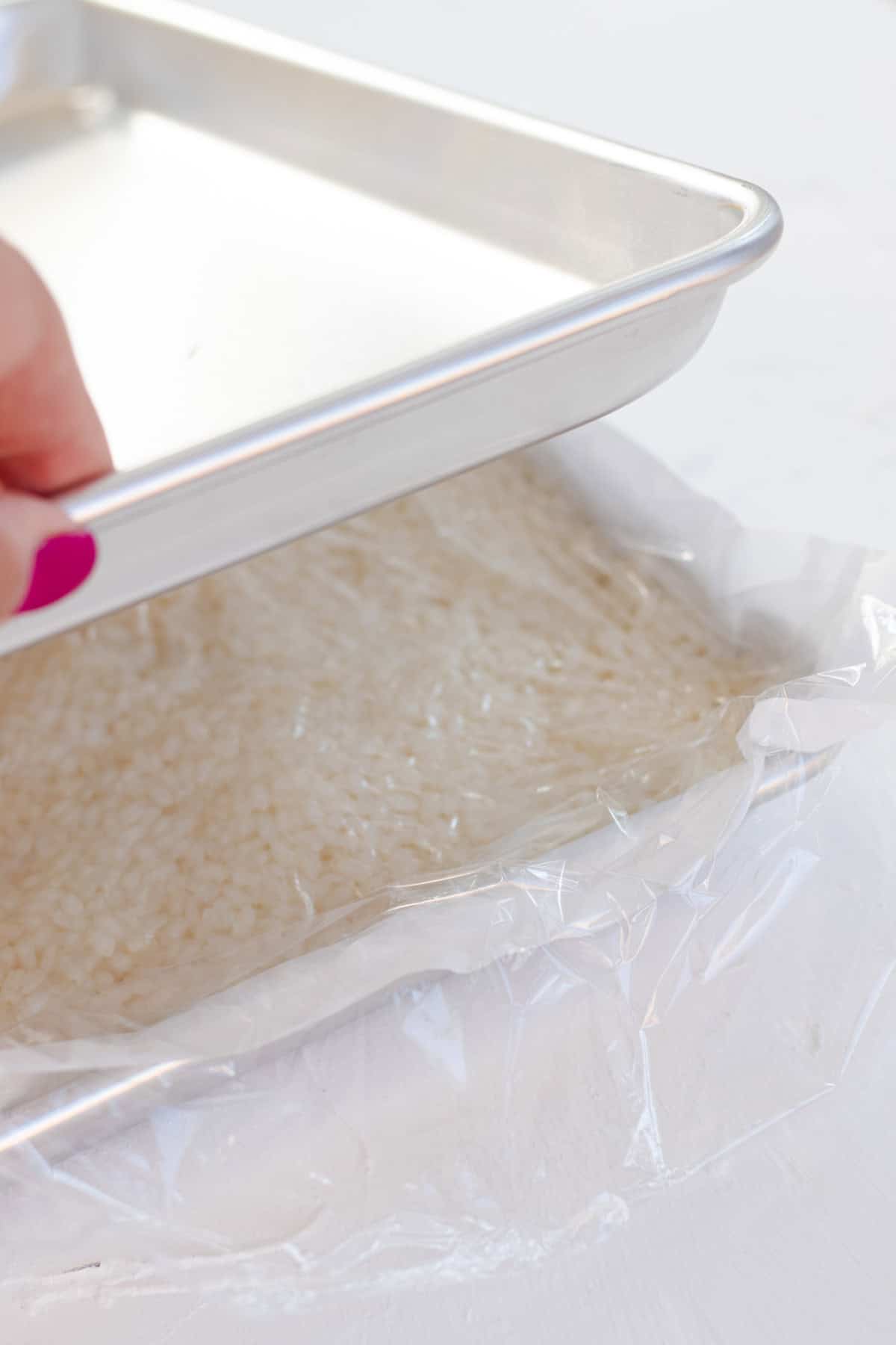Placing plastic wrap overtop of the rice and pressing with a second quarter sheet pan until flat.