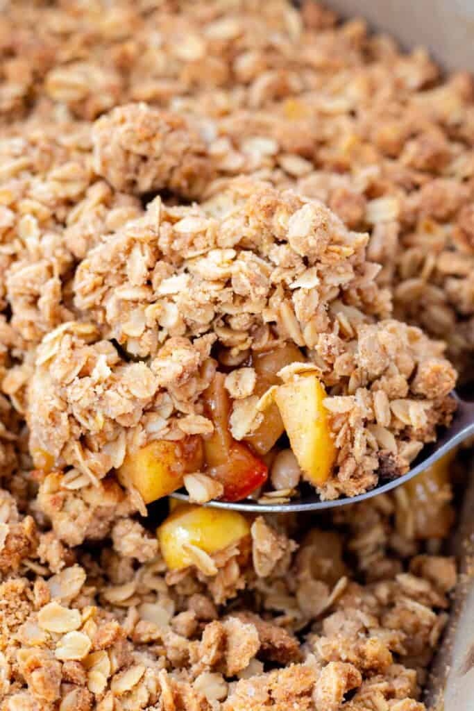 Scooping baked apple crisp with a stainless steel spoon.