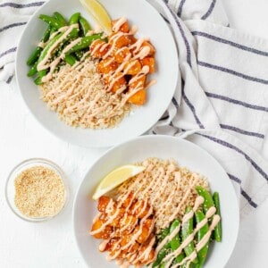 Two fully loaded sweet chili tofu bowls with a bowl of toasted sesame seeds on the side.