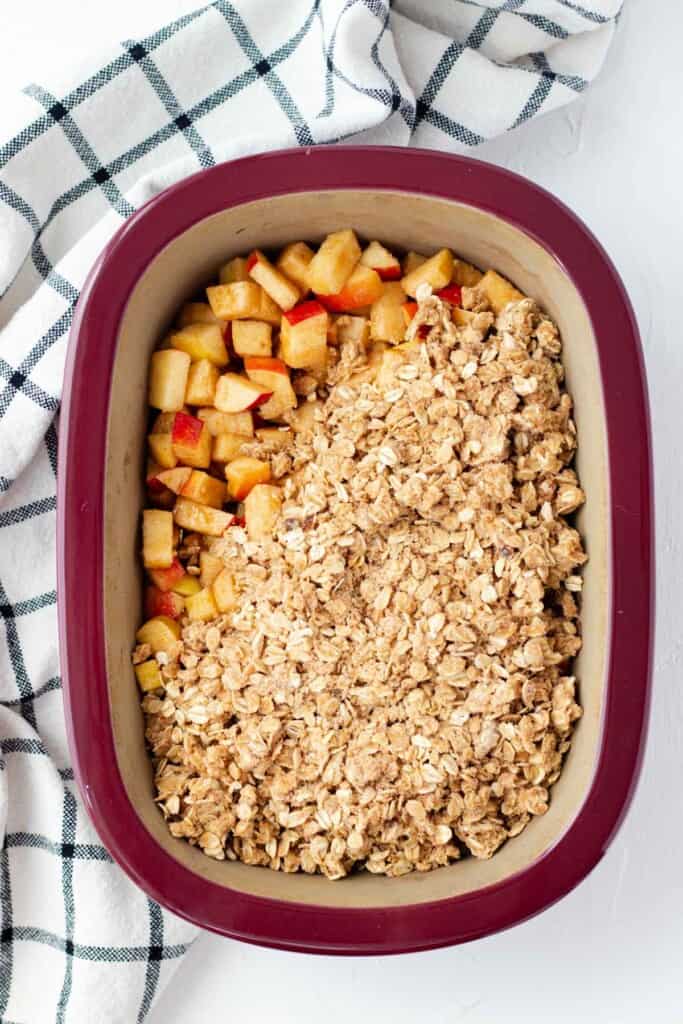 Building the crisp in a baking dish, starting with the spiced apples on the bottom and the buttery crisp topping on top.