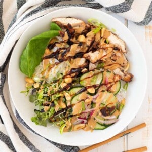 A white bowl of rice vermicelli with grilled chicken, quick pickled cucumber and red onion and all the garnishes.